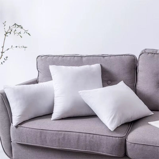 Trois coussins blancs unis posés sur un canapé en tissu gris