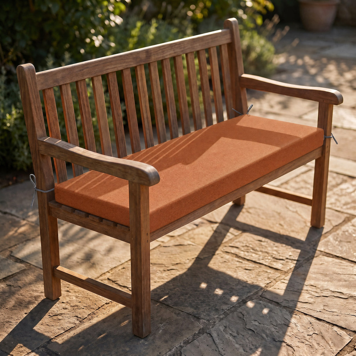 Coussin de banquette sur mesure en polyester coloris terracotta, coussin plat avec cordons d'attache, posé sur un banc de jardin en teck