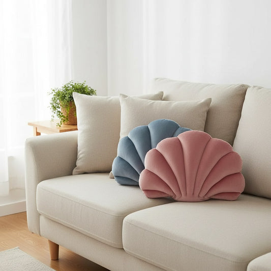 Coussins coquillage en velours vieux rose et bleu lavande devant des coussins beiges sur un canapé