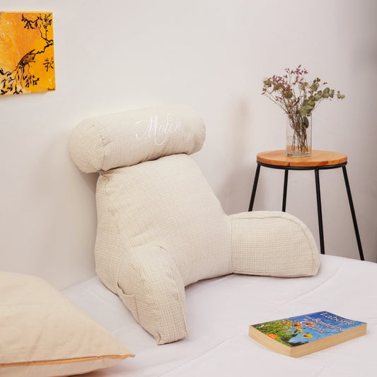 Coussin de lecture ivoire avec accoudoirs et appui-tête posé sur un lit dans une chambre claire
