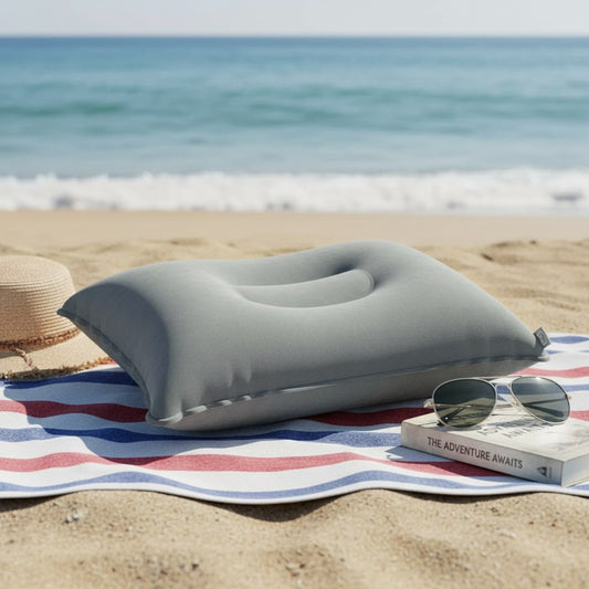 Coussin de plage gonflable gris posé sur une serviette, sur le sable