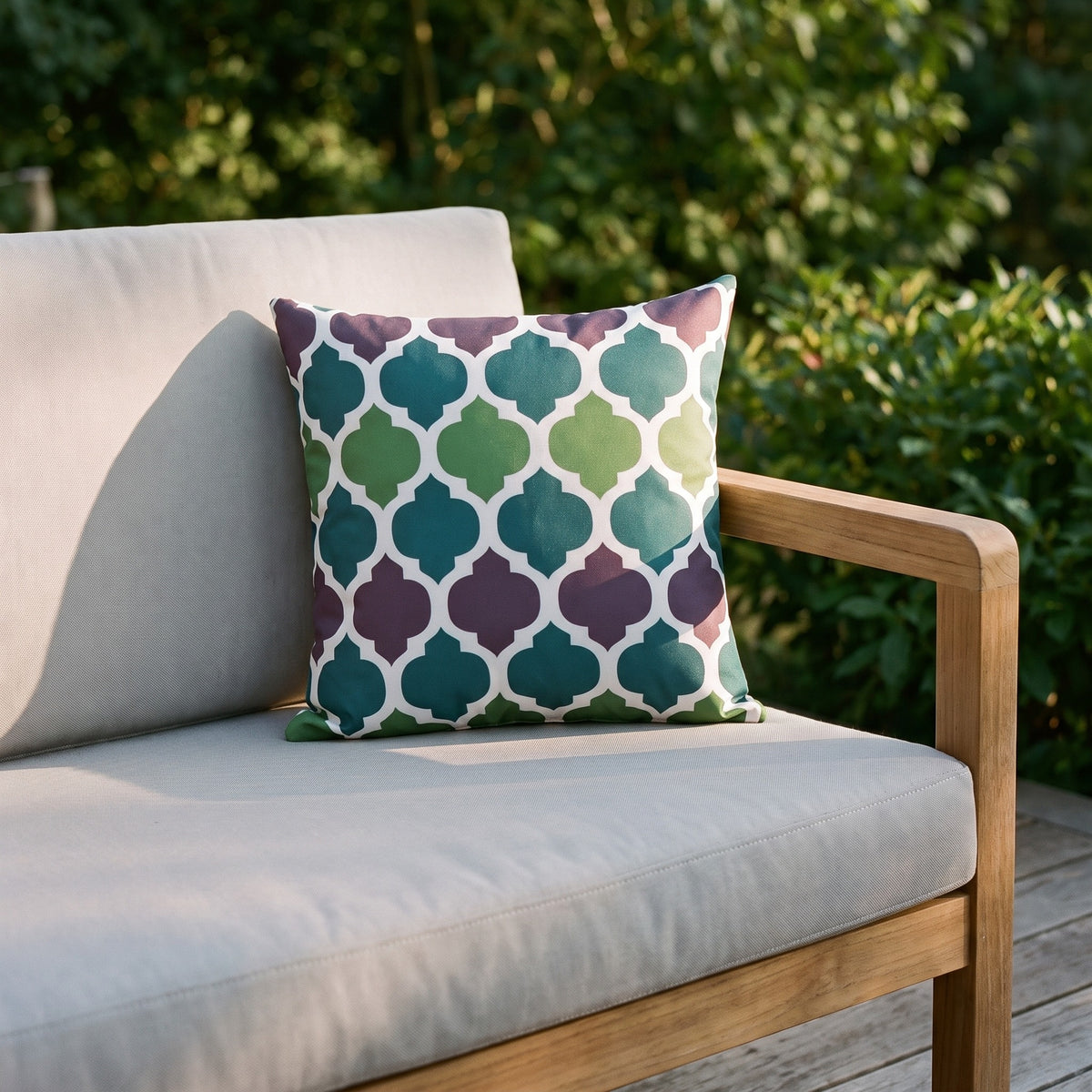 Housse de coussin extérieur imperméable motif Arabesque vert et violet sur un canapé de jardin en teck, terrasse ensoleillée