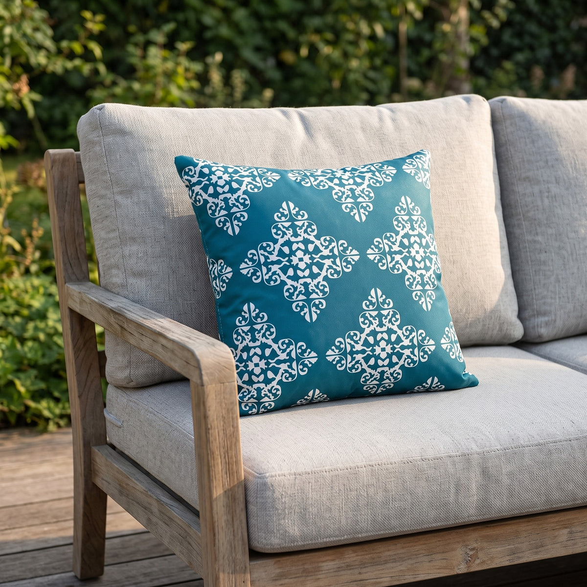 Housse de coussin extérieur imperméable motif Médaillon bleu canard sur un canapé de jardin en teck, terrasse ensoleillée