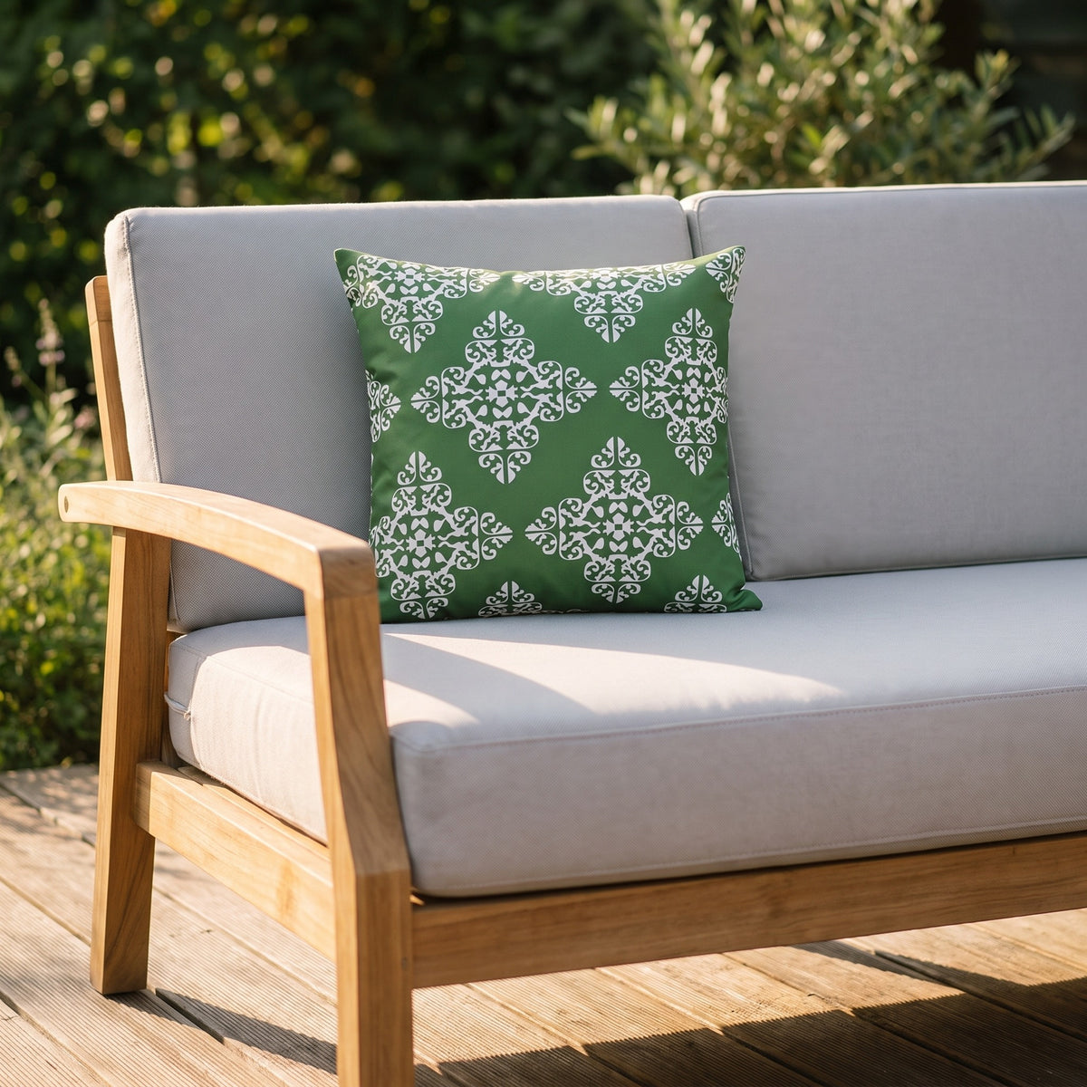 Housse de coussin extérieur imperméable motif Médaillon vert sur un canapé de jardin en teck, terrasse ensoleillée
