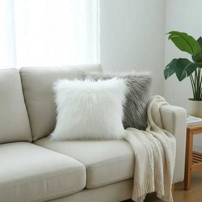 Coussins en fausse fourrure à poils longs blanc et gris sur un canapé, avec un plaid en maille