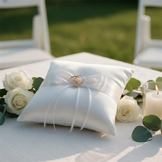 Coussin porte-alliance en satin blanc avec deux alliances, sur une table de cérémonie fleurie