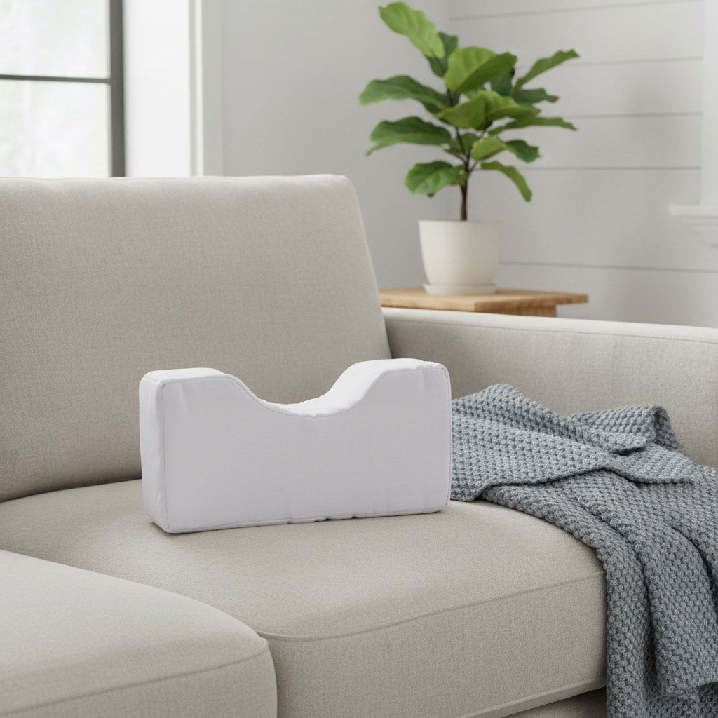 Coussin relève-jambe en U blanc posé sur un canapé
