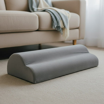 Coussin repose-pieds gris posé sur un tapis devant un canapé