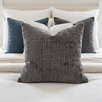 Coussins 50 x 50 cm en chenille bleu jean et gris anthracite devant les oreillers d'un lit blanc