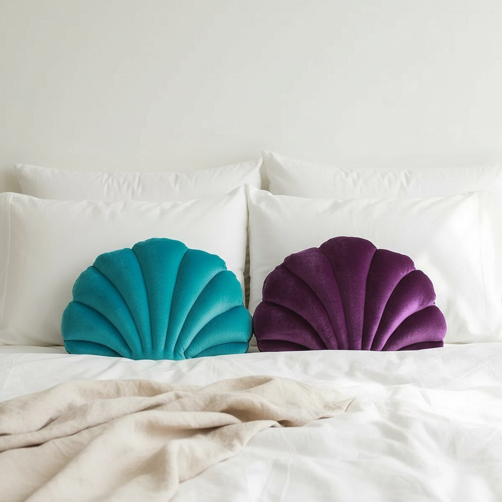 Coussins coquillage en velours turquoise et violet devant les oreillers d'un lit blanc