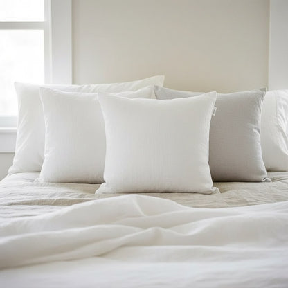 Coussins en lin blanc et gris perle devant les oreillers d'un lit