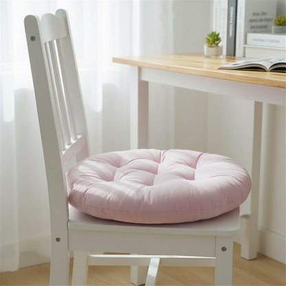 Galette de chaise ronde rose pâle sur une chaise blanche, devant un bureau