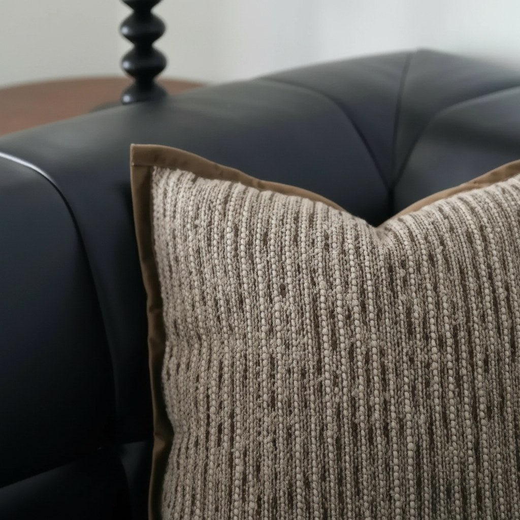 Détail du tissage rayé brun et écru et du bord plat d'une housse de coussin