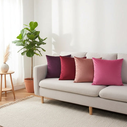 Housses de coussin en velours violet, bordeaux, rose et fuchsia alignées sur un canapé gris clair