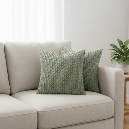 Deux coussins vert sauge en maille texturée en relief sur un canapé blanc