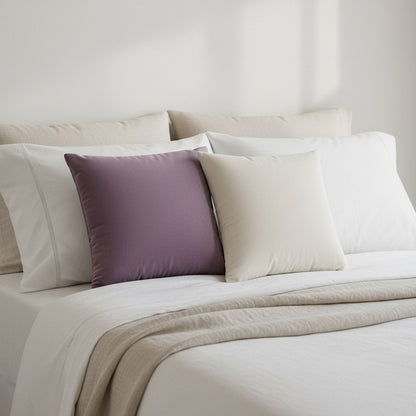 Petits coussins en velours prune et crème devant les oreillers d'un lit